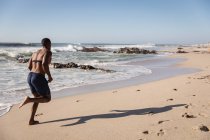 Vista trasera de los jóvenes afroamericanos corriendo en la playa en un día soleado - foto de stock