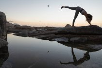 Tiefansicht einer Frau beim Yoga auf einem Felsen am Strand bei Sonnenuntergang — Stockfoto