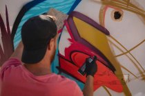 Vue arrière du jeune artiste graffiti caucasien peinture par pulvérisation sur une pièce murale altérée — Photo de stock