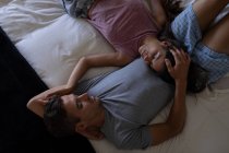 Высокий угол обзора романтической многонациональной пары, смотрящей друг на друга, лежа дома на кровати — стоковое фото