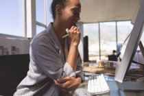 Вид сбоку на молодую бизнесвумен смешанной расы, работающую за компьютером на рабочем столе в офисе — стоковое фото