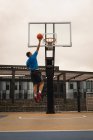 Vue arrière d'un joueur de basket marquant un cerceau sur un terrain de basket contre un bâtiment en arrière-plan — Photo de stock