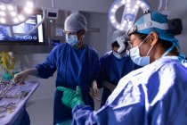 Side view of surgeons concentrated in operating room during surgery while they are choosing tools at hospital — Stock Photo