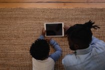 Высокоугольный вид отца и сына афроамериканцев, использующих цифровую планшет, лежа дома на ковре — стоковое фото
