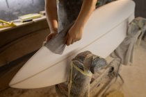 Partie médiane de l'homme nettoyant la planche de surf avec un chiffon dans un atelier — Photo de stock