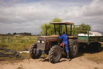 Rückansicht eines afrikanisch-amerikanischen Farmers in Anzug, der auf einem Wirtschaftsweg auf einen Traktor steigt — Stockfoto