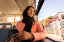 Tieffliegerblick einer nachdenklichen Frau mit gemischter Rasse, die durch das Fenster des Busses blickt, während sie darin reist — Stockfoto