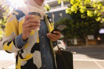 Low angle view of woman using mobile phone while holding a coffee in the street on a sunny day — Stock Photo