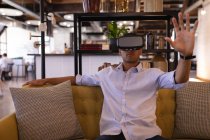Вид спереду гарний бізнесмен змішаної раси з використанням гарнітури віртуальної реальності, що сидить в сучасному офісі — стокове фото