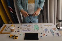 Mid section of man taking photo of surfboard sketches with mobile phone in workshop — Stock Photo