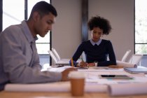 Frontansicht fokussierter junger Geschäftsleute mit gemischter Rasse, die in einem Besprechungsraum mit Bleistiften an Plänen arbeiten — Stockfoto