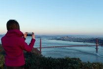 Rückansicht einer Frau beim Fotografieren einer Brücke an einem sonnigen Tag — Stockfoto