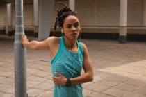 Frontansicht einer jungen Frau mit gemischter Rasse, die während ihres Trainings in der Stadt Musik über Kopfhörer hört — Stockfoto