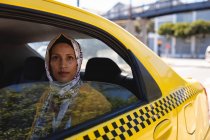 Вид спереду вдумлива змішана раса жінка дивиться на камеру, сидячи в таксі в сонячний день — стокове фото