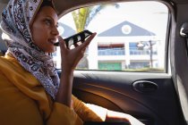 Vue latérale de belle femme mixte parlant sur haut-parleur de téléphone mobile tout en voyageant en voiture par une journée ensoleillée — Photo de stock