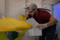 Side view of Caucasian man applying yellow sanded matt on the surfboard in surf shop. — Stock Photo
