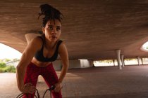 Vue de face de la jeune femme de race mixte se reposant après l'exercice sous un pont dans la ville — Photo de stock