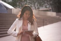 Вид на азіатську жінку з використанням цифрової таблетки, стоячи на тротуарі в сонячний день — стокове фото