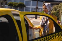 Vue de face de femme métissée réfléchie monter dans le taxi dans la rue — Photo de stock