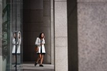 Вид збоку молода красива Азіатська жінка говорити на мобільному телефоні під час прогулянки по коридору — стокове фото