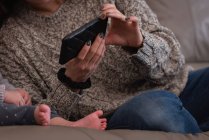Средний вид на мать и дочь с помощью мобильного телефона, сидя на диване дома — стоковое фото