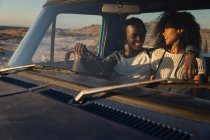 Vista frontal do romântico jovem casal afro-americano relaxando em um carro em um dia ensolarado — Fotografia de Stock