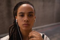 Porträt einer jungen Frau mit gemischter Rasse, die auf der Straße über Kopfhörer Musik hört — Stockfoto