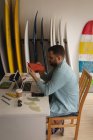 Vue latérale de l'homme caucasien examinant la nageoire de planche de surf dans un atelier — Photo de stock
