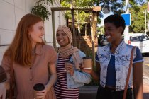 Вид спереду на щасливу молоду змішану расу друзі-жінки взаємодіють один з одним, маючи каву на вулиці — стокове фото