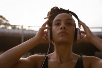 Primer plano de la joven mujer de raza mixta escuchando música en los auriculares de la ciudad - foto de stock