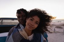 Vista frontal do casal romântico afro-americano apoiando-se no carro na praia ao pôr do sol — Fotografia de Stock