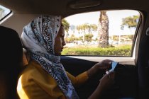 Vista lateral da bela mulher de raça mista usando telefone celular enquanto viaja de carro — Fotografia de Stock