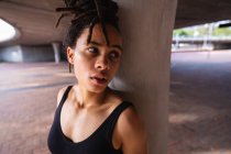 Porträt einer jungen Frau mit gemischter Rasse, die nach dem Sport unter einer Brücke in der Stadt ruht — Stockfoto