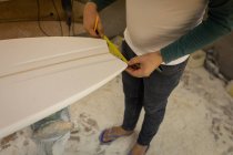 Section basse de l'homme mesurant l'extrémité d'une planche de surf dans un atelier — Photo de stock