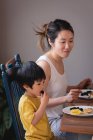 Vista lateral de uma mãe e filho asiáticos desfrutando de café da manhã na mesa de jantar na cozinha em casa — Fotografia de Stock