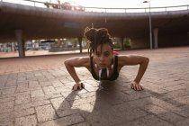 Visão frontal de apto jovem mulher de raça mista fazendo exercício push-up na cidade — Fotografia de Stock