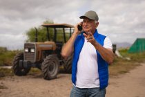 Frontansicht eines älteren kaukasischen Bauern, der am sonnigen Tag auf einem Bauernhof mit dem Handy telefoniert — Stockfoto