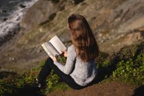 Vue arrière d'une belle femme lisant un livre assis sur une pente de montagne — Photo de stock