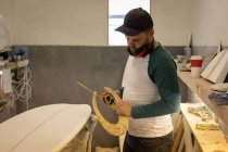 Vue latérale de l'homme caucasien mesurant la planche de surf avec règle spéciale dans un atelier — Photo de stock
