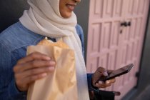 Parte centrale di una donna di razza mista che usa il cellulare mentre fa colazione per strada — Foto stock