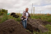 Frontansicht eines aktiven Senior-kaukasischen männlichen Bauern mit Schaufel, der auf dem Feld auf dem Bauernhof gräbt — Stockfoto