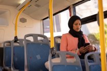 Vista frontal da bela mulher de raça mista usando telefone celular enquanto viaja em ônibus — Fotografia de Stock