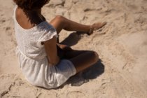 Високий кут зору змішаної раси жінка сидить на піску, розслабляючись на пляжі на сонячному — стокове фото
