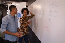 Seitenansicht glücklicher junger Geschäftsleute mit gemischter Rasse, die im modernen Büro stehend und angelehnt miteinander interagieren — Stockfoto