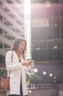 Низький кут зору азіатських жінок за допомогою мобільного телефону, стоячи на вулиці — стокове фото