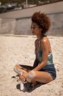 Вид збоку на молоду змішану жінку, яка розслабляється на пляжі, тримаючи в руці сонячний лосьйон . — стокове фото