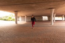Front view of young Mixed race woman running under a bridge in the city — Stock Photo