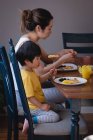 Вид сбоку на мать и сына азиатского происхождения, которые завтракают на обеденном столе на кухне дома — стоковое фото