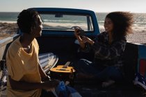Side view of African American woman capturing photo of African American man while sitting at car on beach on sunny day — Stock Photo