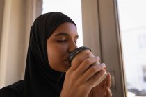 Perfil de una hermosa joven en hijab tomando café en una cafetería - foto de stock